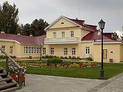 A peach-colored prune-tiled three-story house with single-story aisles surrounded by trees