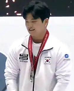 A Korean man wearing a white top with the South Korean flag on it and a red lanyard.
