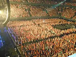 Fans at a concert with their arms stretched above their heads. The image is taken from above.