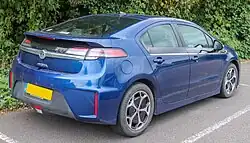 Rear 3/4 view of a dark blue automobile with trees in the background and a UK licence plate