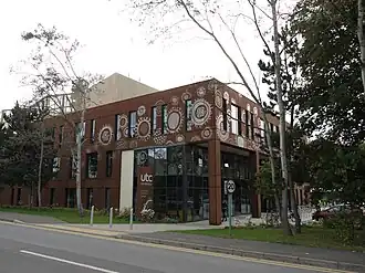 A modern, cuboidal building with rust-brown metal walls decorated with large white cogwheel motifs