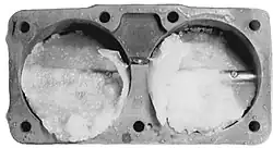 A metal rectangular carburetor with two large boreholes. There is visible ice accumulation inside each borehole
