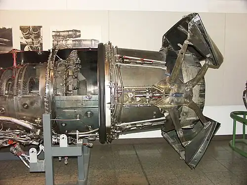 Low bypass turbofan (Turbo-Union RB199) with afterburner. Visible at the left is the bypass duct surrounding the turbines. For the afterburner can be seen the bypass fuel injectors and bypass flame holders and core flameholder in the centre. The core fuel injection is unseen upstream. Reliable burning in the bypass air, which can be as cold as 300&nbsp;K, is guaranteed by collecting some of the turbine exhaust stream to heat the bypass flameholders. The buckets shown half-way between deployed and stowed positions are for the thrust reverser.