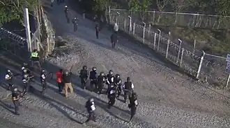 fifteen uniformed guards pointing guns at people moving away down road