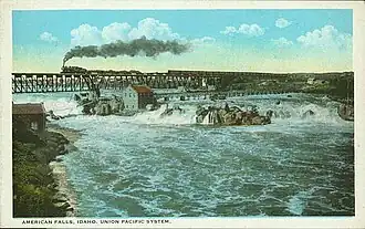 A painted postcard shows a train crossing a bridge above a wide waterfall and turbulent river.