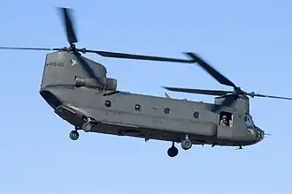Colour photo of a dark green twin-rotored helicopter in flight