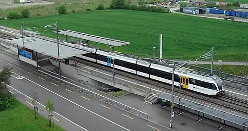 White train with black stripe pulling out of a station with two side platforms