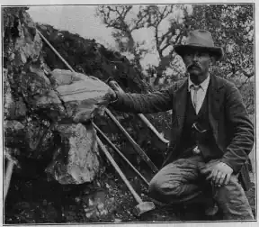 William E. Hidden next to a 73&nbsp;lb (33&nbsp;kg) mass of gadolinite in place at Barringer Hill, 1903.