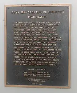 Black plaque with gold trim and text. Plaque reads: "Dona Bernarda Ruiz de Rodriguez Peacemaker. Adjoining this site resided Bona Bernarda Ruiz de Rodriguez, a woman highly respected, with extensive family ties and strong political connections. Her negotiations with Lt. Col. John C. Fremont at the Alpheus B. Thompson house next door, to attain a "peace, acceptable and enduring" by compromise, brought an end to the Mexican-American War in California with the signing of the Treaty of Cahuenga in 1847. This was a major step that brought California into the American Union. Lt. Col. Fremont and his officers were quartered at the Thompson House from Dec. 27, 1846 to Jan. 3, 1847. Mr. Thompson, a prominent Santa Barbara citizen and china trader, built his house in 1834 for his bride, Francisca Carrillo, cousin of Bernarda Ruiz. The house became known as the San Carlos Hotel, later the St. Charles. Plaque dedicated by Santa Barbara Parlor no.116, Reinda del Mar Parlor No.126, Tierra de Oro Parlor No. 304 Native Sons and Daughters of the Golden West. June 26, 1975"