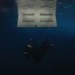 In the dark depths underwater, a clothed Billie Eilish sinks. At the top, a white door on the surface opens downwards.