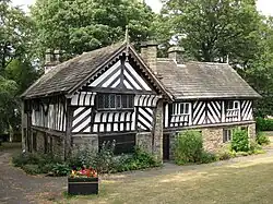Photograph showing a timber-framed house. There are two sections to the building at right angles to each other forming a T shape. The ground level of the building has stone walls, whereas the upper floor has wattle and daub infill.