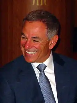 A man in a blue suit and a blue tie looks to his right and smiles.