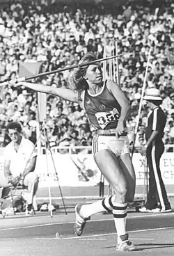 A light-skinned woman, with her right arm extended backwards, holding a javelin
