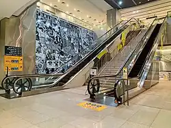 Two escalators with a stair in between them and a mural behind the one further away