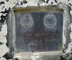 A grey plaque on a white surface with evidence of chipped paint and general decay