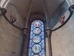 A semi-circular area with stone walls, a domed ceiling and a tall stained glass window with prominent circular decorations.