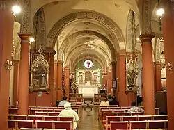 A view down the nave towards the altar. Smooth red columns support cream arches with grey-blue floral decorations. There is a round window above the altar.