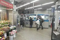 View of the fare control area at ground level. There is a station agent booth in the background and a florist to the left.
