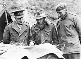 Three men study a map. They are wearing military uniforms, with a peaked cap, a slouch hat and a beret, but are dressed warmly against the cold with scarves and gloves.
