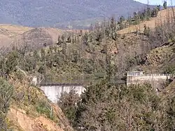 Waterfall surrounded by stone walls in brown wooded hills; many of the standing trees are barren, gray, and dead.