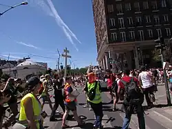 A counter-protester at the Budapest Pride 2025 event holding up a two-barred cross, surrounded by press and event organizers