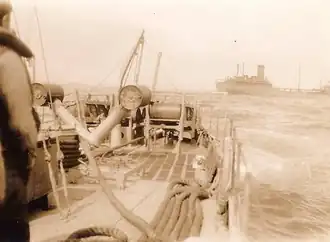 An oil tanker is half-visible just behind the stern of Dione; the tanker is partially cut out by the camera's frame