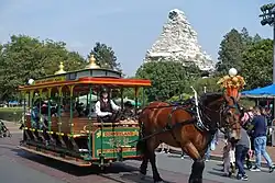 A green and yellow open-air horse-drawn streetcar hitched to a draft horse