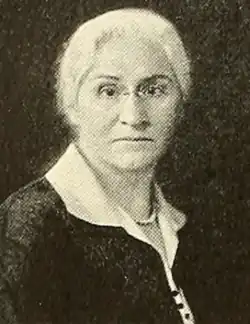 A middle-aged white woman with white hair, wearing glasses