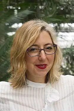 Kapsalis is looking toward the camera with a slight smile and holding an outstanding service award.