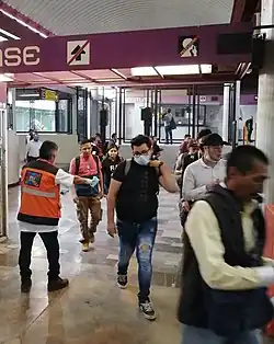 Several people, some wearing masks and others not, walk through a lobby.