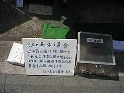 A sign with Japanese characters next to a donation box with coins inside