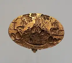 A gold ring, like the Ring of Nestor, with an oval bezel inscribed with figures. A youth climbs a hill in the centre to pick something from a tree, while two seated female figures watch.