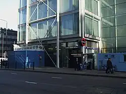 A building covered in windows with a blue sign reading "EUSTON SQUARE STATION" in white letters all under a blue sky with white clouds