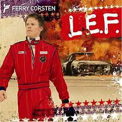 Ferry Corsten, seen wearing a racing suit, leaves out of a car which is seen burning on fire.