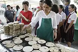 A photograph of a woman cooking pupusas