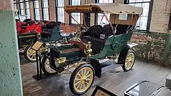 A green-colored, old-fashioned car with four seats and brass fittings
