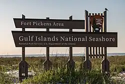 Wooden sign saying "Fort Pickens Area, Gulf Islands National Seashore" standing in front of a beach at sunset