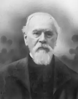 Black and white bust-length photoportrait of Nau, wearing a black suit