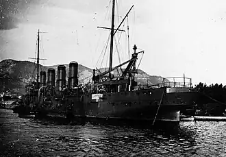 A large gray ship in port, with coal being loaded by a large crane directly behind it.
