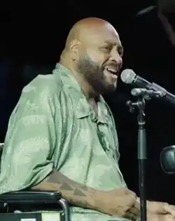 bald portly polynesian man in a wheelchair performing