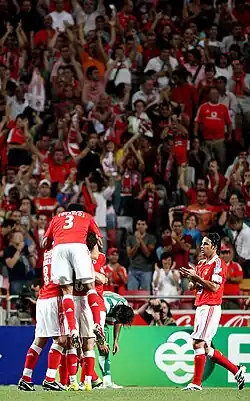 Players celebrating a goal in front of fans wearing red, the team color