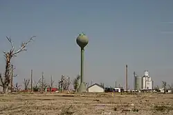 A green water tower is seen surrounded by tornado damage, including debarked trees.