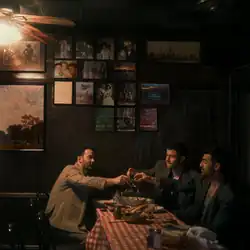 The band members sitting at a diner and toasting. Above them are multiple frames and pictures.