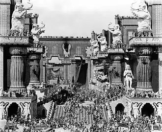 A large-scale movie set depicting ancient Babylonian gates with towering walls, ornate columns, and decorative elephant statues