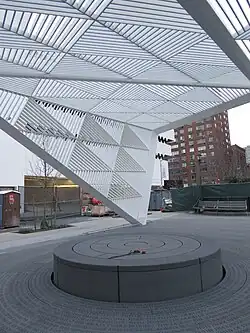 Image of the HIV AIDS NYC monument. A concrete oblate cyinder sits on the ground with a white overhang barely touching it.