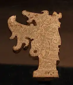 A piece of ancient jade jewelry carved into a face. It is behind glass in a museum case