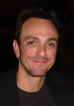 Head shot of broadly smiling man in black with receding dark hair and a day's beard growth on his face.