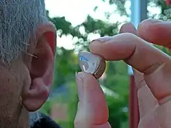 Close-up photograph of a person holding a hearing aid close to their left ear