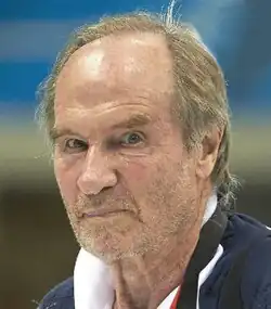 Colour, three-quarter profile press shot of an unshaven man with receding, greying hair.