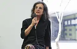 A woman of middle age sitting holding a microphone in her hand.
